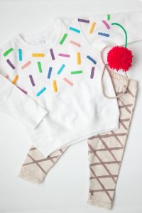 Tan Pants with Brown Cross Marks, White Sweater with colored rectangles, Red Puffy Ball with Green Stem