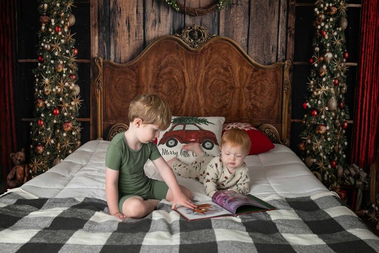 holiday Christmas sessions with a bed set up and holiday pajamas reading a Christmas story book