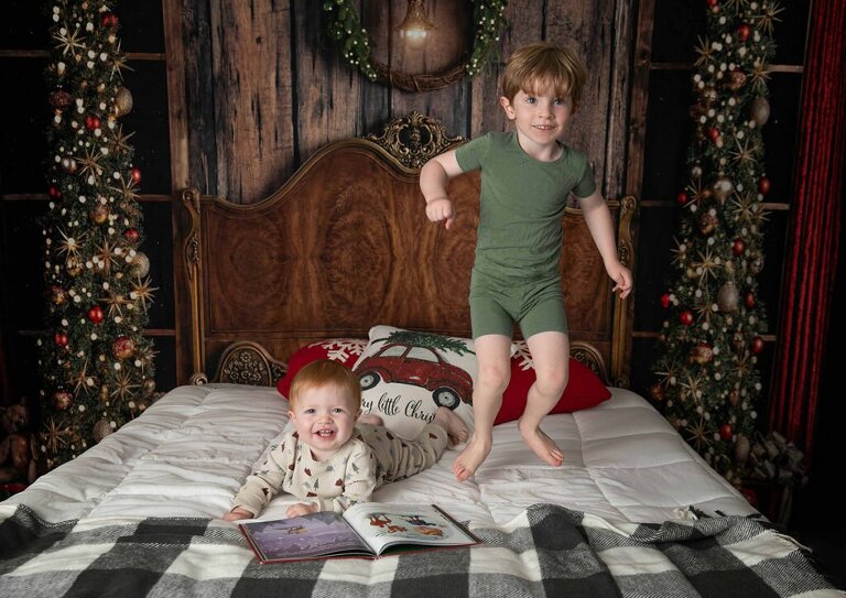 holiday Christmas sessions with a bed set up and holiday pajamas. 2 little boys jumping on the bed and reading holiday stories